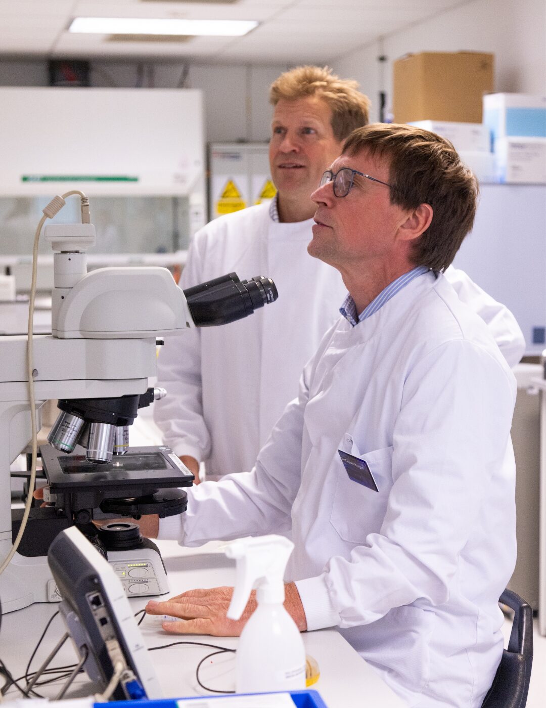 Professors Hywel Morgan and Paul Elkington using a microscope in a laboratory